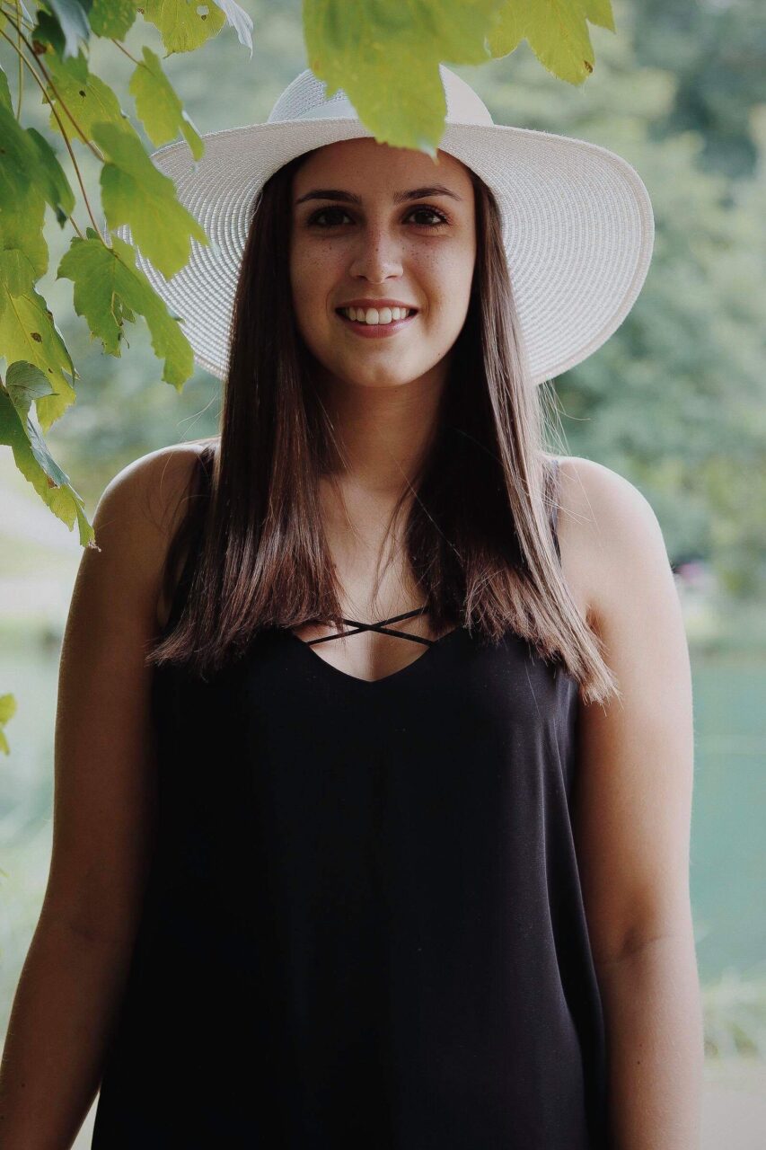 Caroline Mertz en chapeau blanc, sous les feuillages (2018)