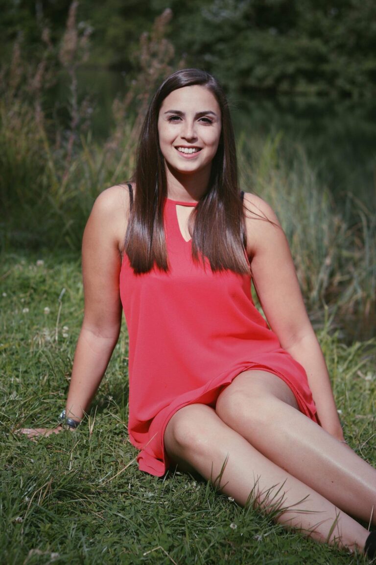 Caroline Mertz en robe corail, assise dans l’herbe (2018)