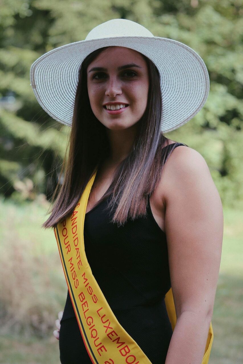 Caroline Mertz en chapeau blanc et robe noire, avec son écharpe de candidate (2018)