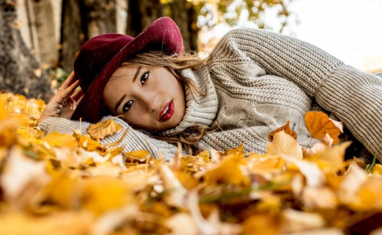Stéphanie Simoens en chapeau bordeaux, allongée dans les feuilles d’automne