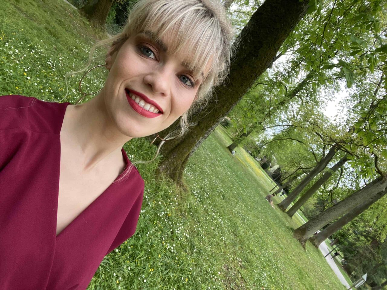 Hélène Henrion en haut bordeaux, autoportrait dans un parc (2021)