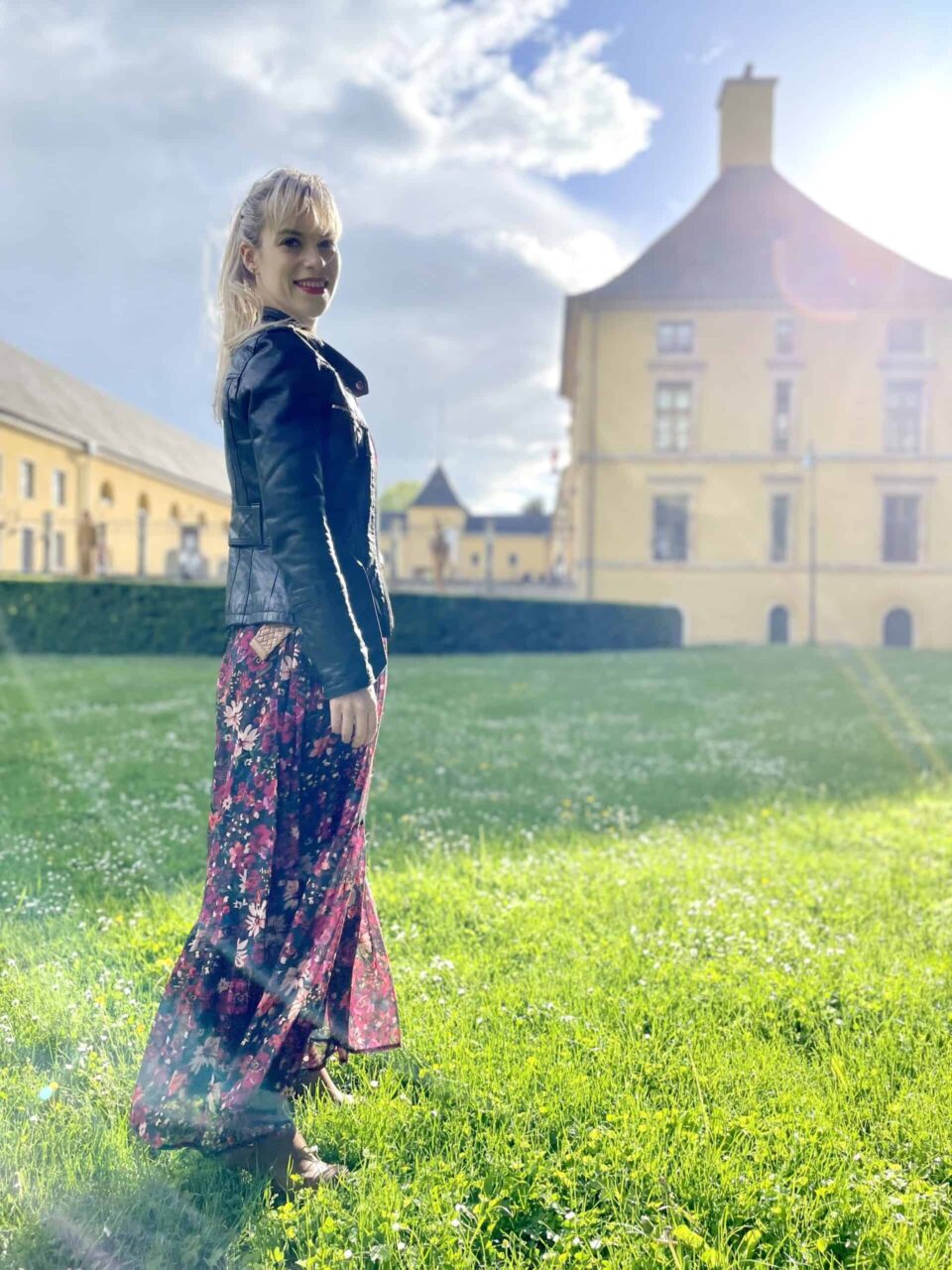 Hélène Henrion en jupe longue fleurie et veste de cuir, sur la pelouse du château (2021)