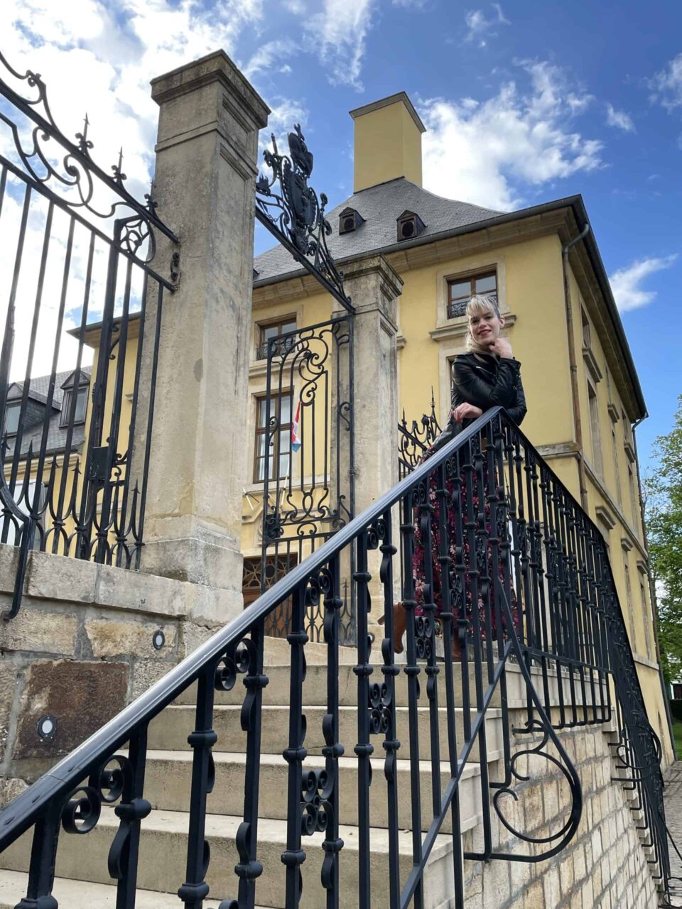 Hélène Henrion sur le perron du château, derrière la grille (2021)