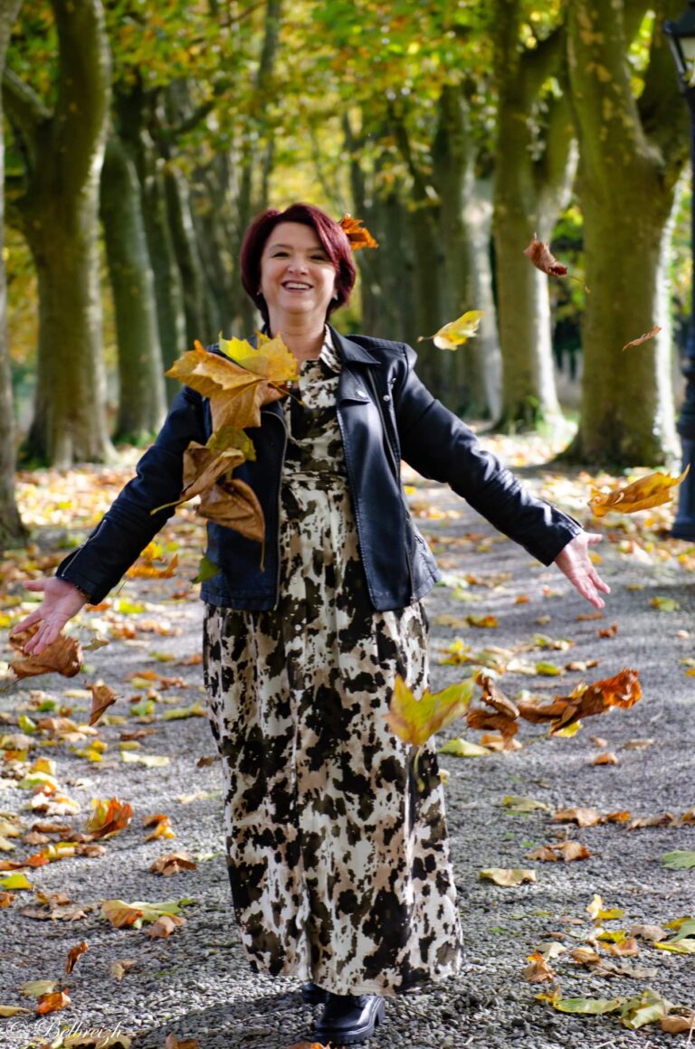 Véronique lance des feuilles d’automne dans une allée