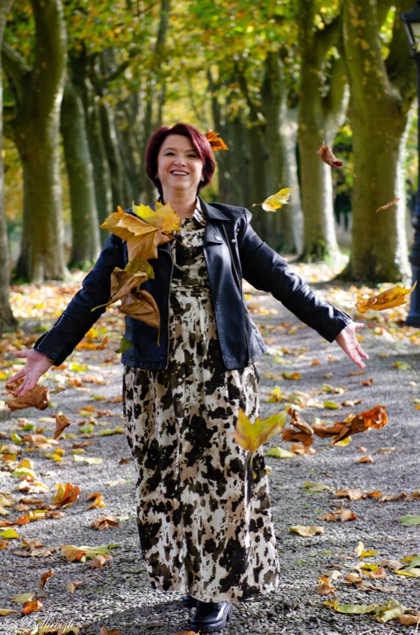 Véronique lance des feuilles d’automne dans une allée