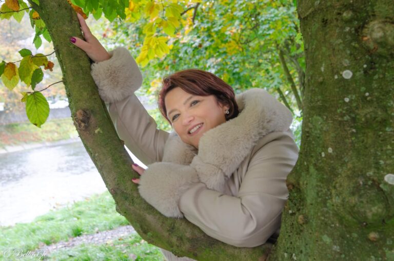 Véronique en manteau clair, accrochée à un arbre au bord de l’eau