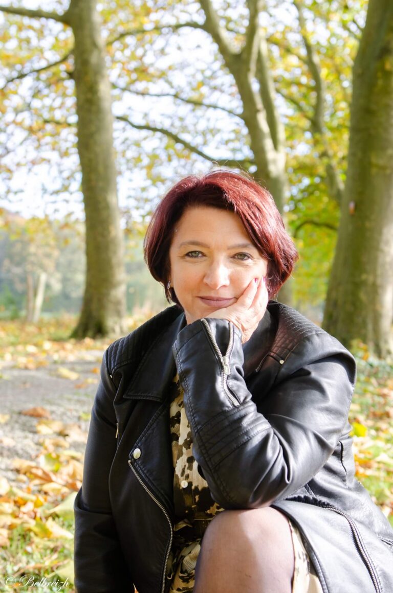 Véronique en veste de cuir, le menton dans la main, dans une allée d’arbres