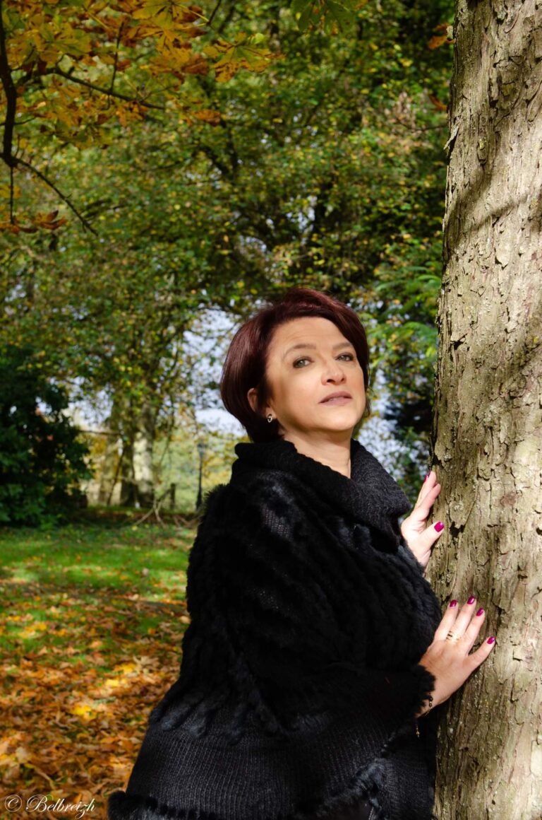 Véronique en noir, contre un tronc d’arbre