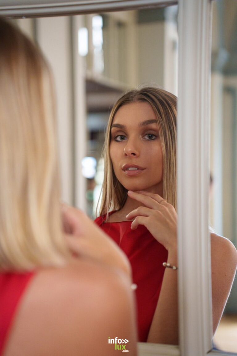Ilona Parison en robe rouge, à travers un cadre de miroir