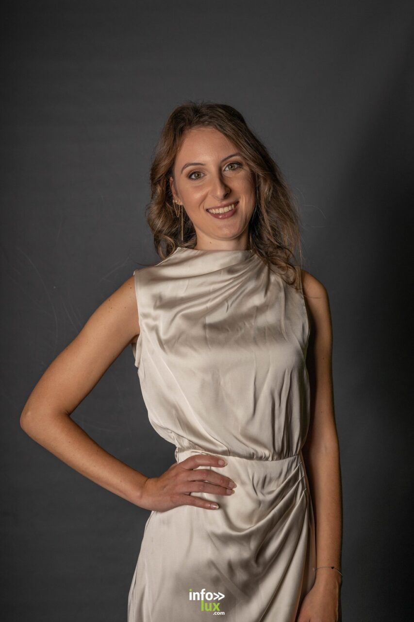 Emilie Gomes en robe de satin ivoire, main sur la hanche, sur fond sombre