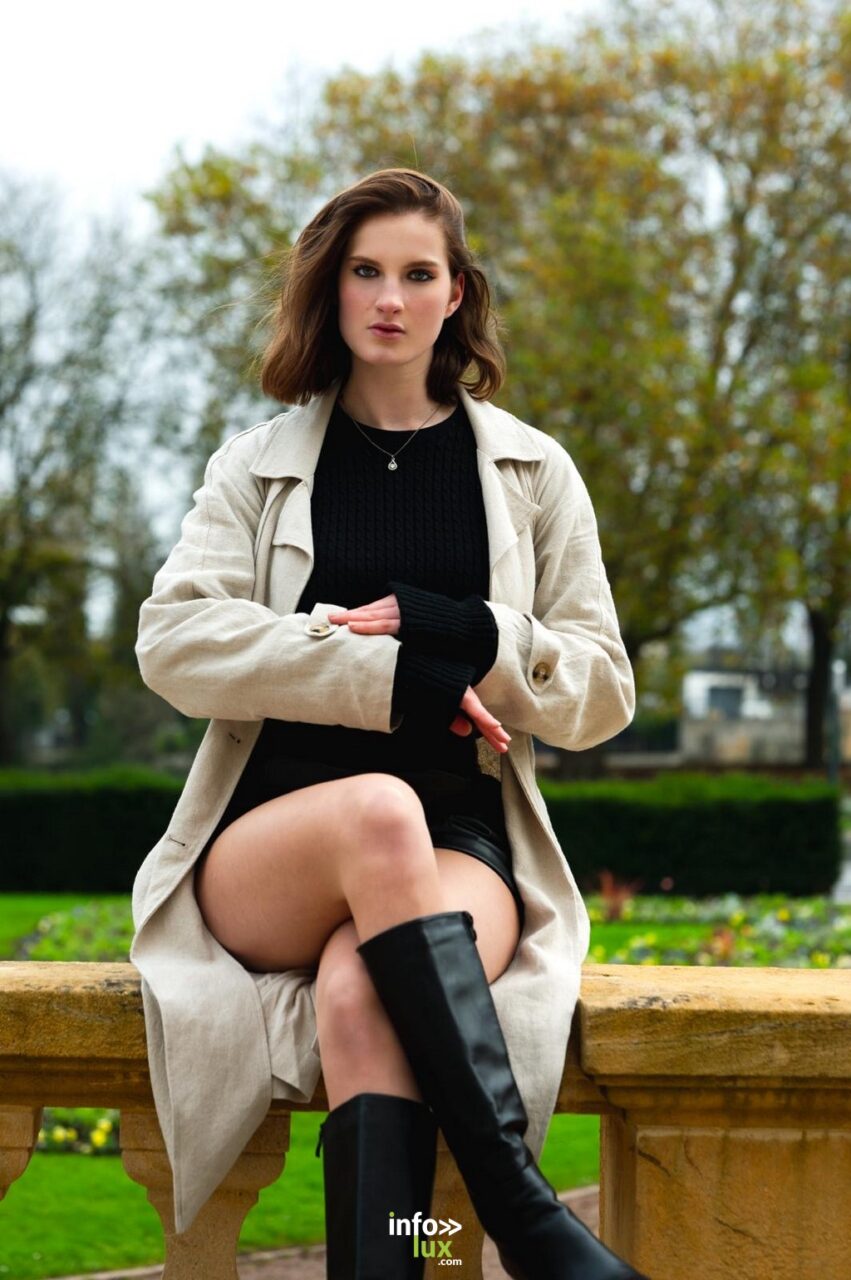 Léanne Stéphano en trench beige et bottes noires, assise sur un muret
