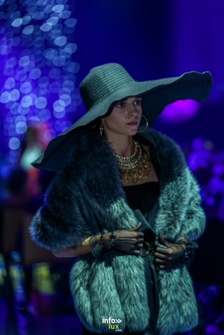 Cécile Ponzellini, grand chapeau et fourrure verte, sous des lumières bleues