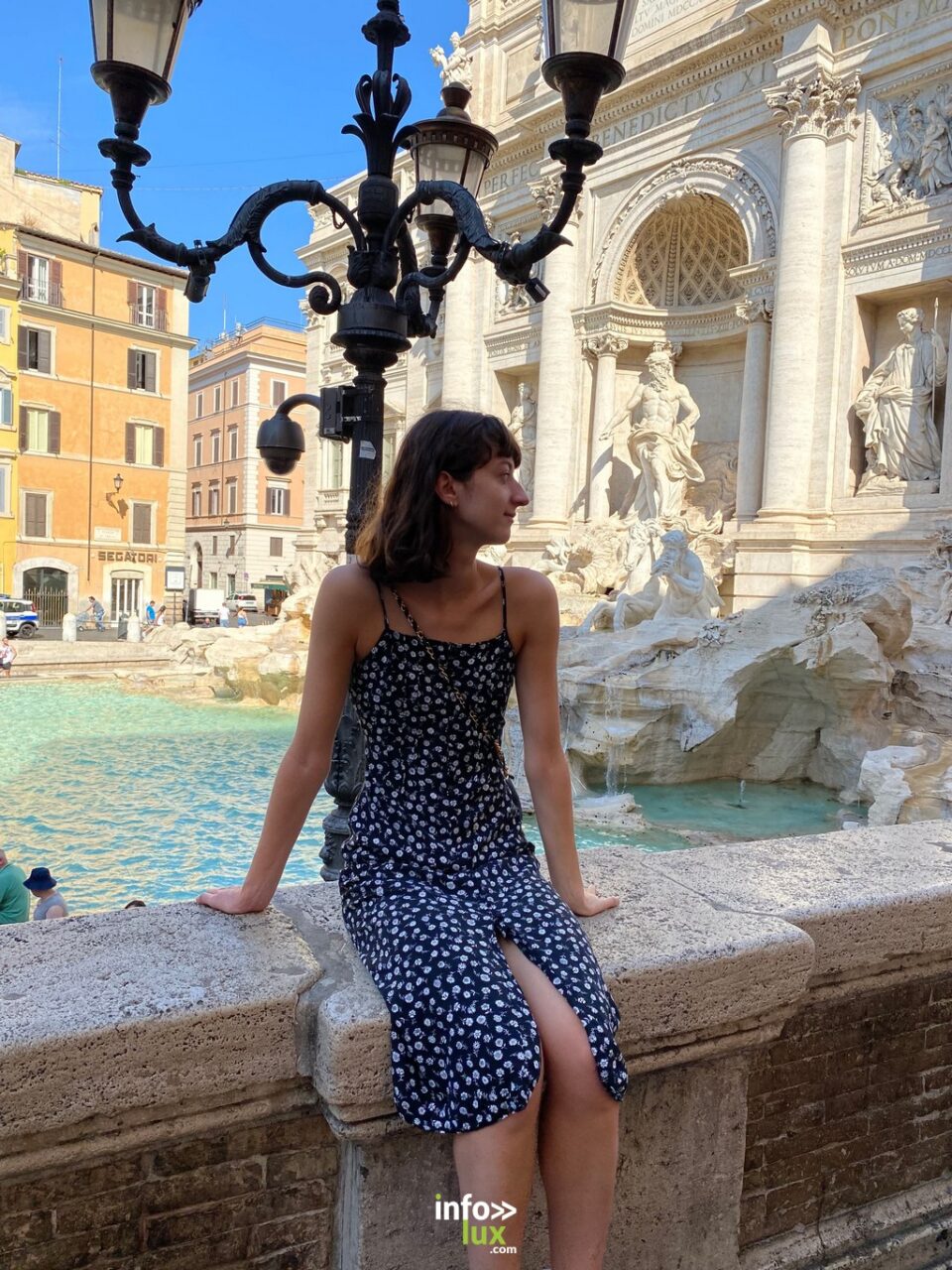 Elisabeth Maire en robe à pois, assise au bord d’une fontaine monumentale