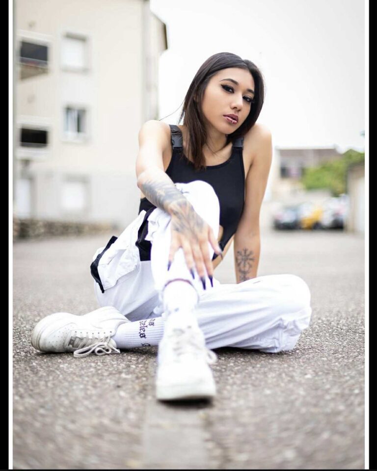 Lou, assise sur le bitume, pantalon blanc et baskets
