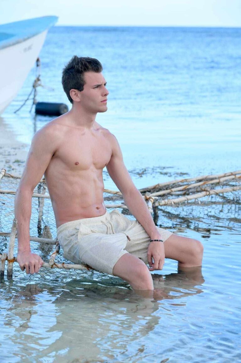 Timothy Legros assis dans l’eau turquoise, près d’une barque