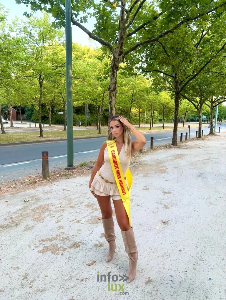 Isaline Dubois en bottes et écharpe de candidate, sur une avenue arborée