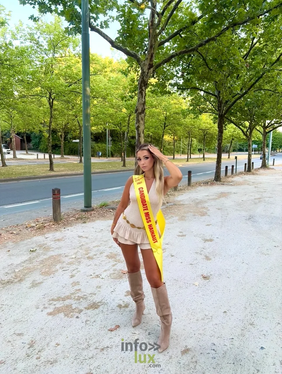 Isaline Dubois en bottes et écharpe de candidate, sur une avenue arborée