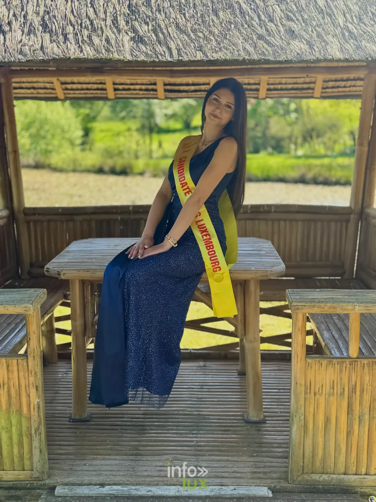 Lola Saquet en robe longue bleu nuit, assise sous un abri de bois