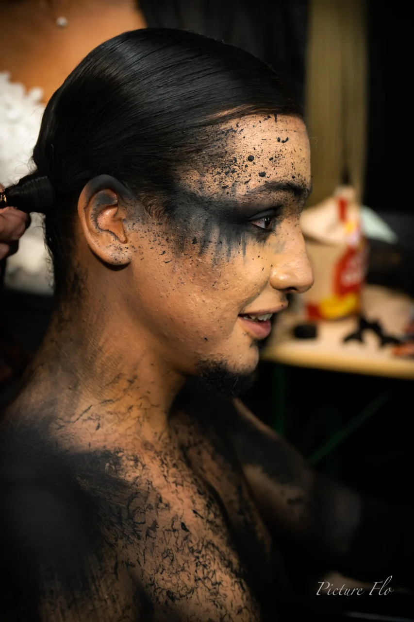 En coulisses : maquillage noir craquelé sur le visage et le torse, longue natte
