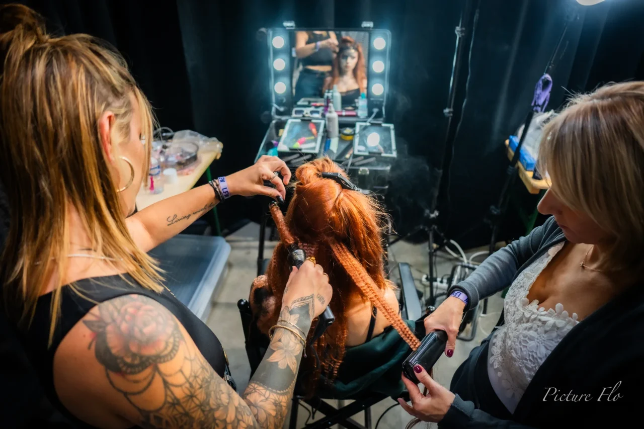 Deux coiffeuses sur une même chevelure rousse, devant un miroir lumineux