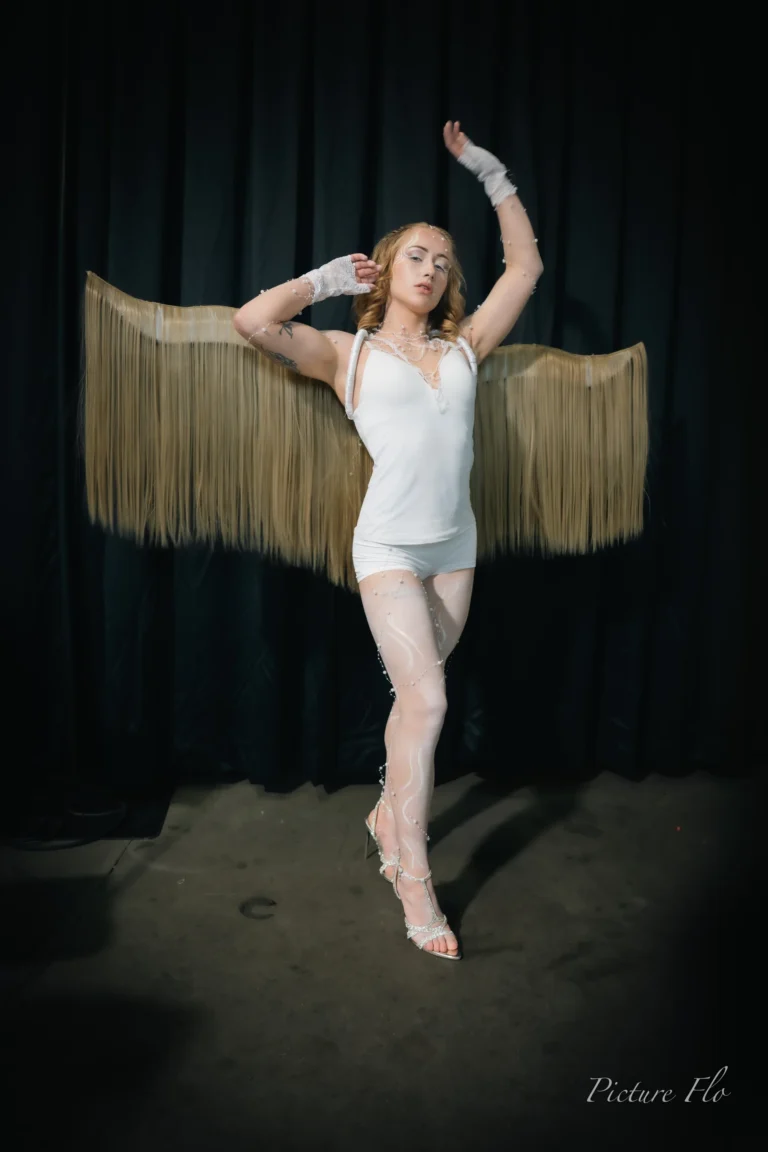 In the studio, one arm raised, the fringed wings behind her