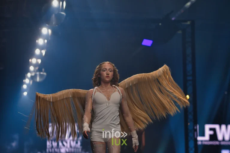 Nova, en body blanc avec des ailes dorées à franges, sur le podium, Lux Fashion Week 2026, Arlon