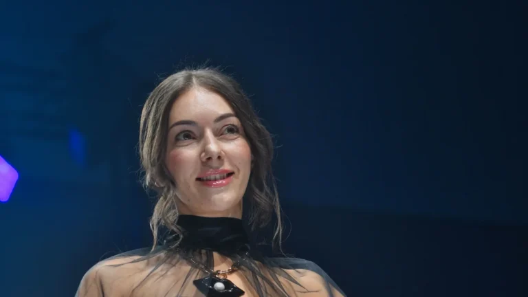 Blouse noire transparente à manches bouffantes, bandeau noir, jupe portefeuille en dentelle crème et or, ceinture de satin doré — Tania Zorina, « Élégance Florale », Lux Fashion Week 2026, Arlon